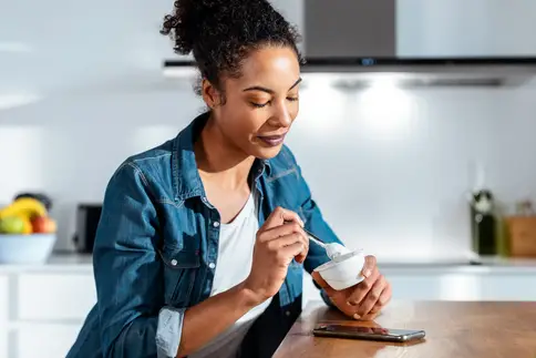 photo of 30s woman eating small cup of yogurt as afternoon snack