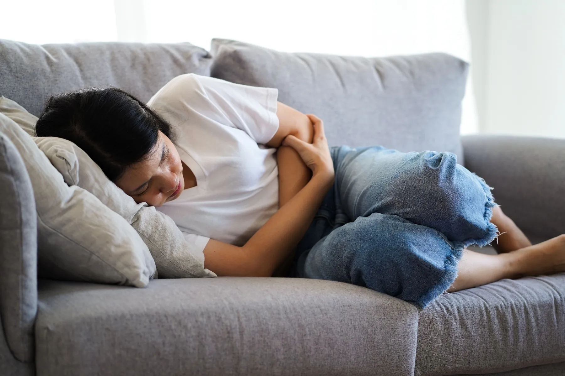 photo of woman crouched on couch holding stomach in pain