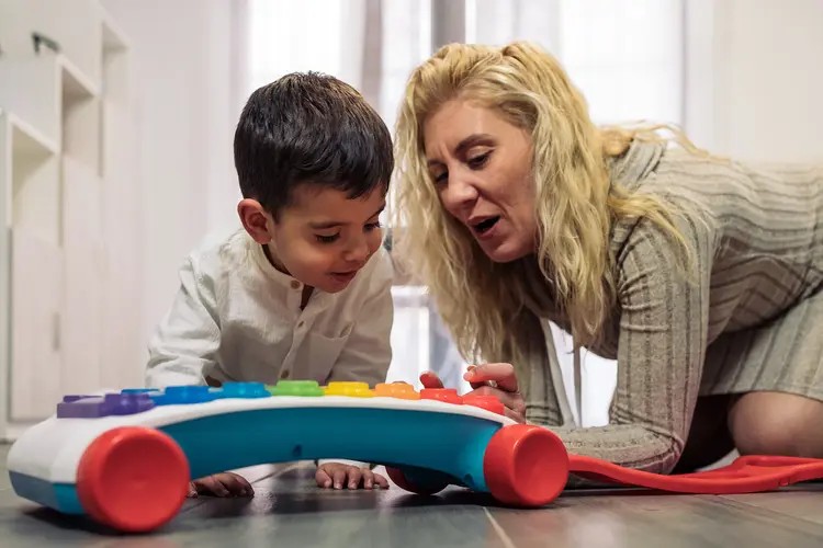 A photo of a woman showing a toddler how to play with a toy instrument