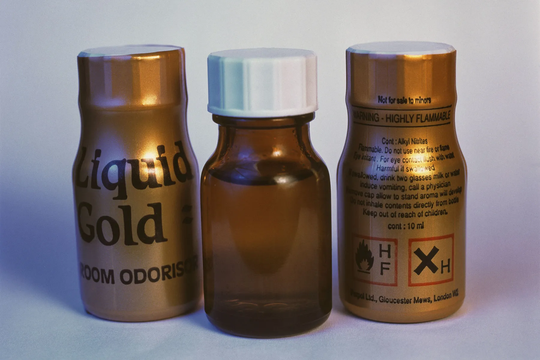 Three small cylindrical bottles of Liquid Gold room odorizer with warning labels, representing popper products