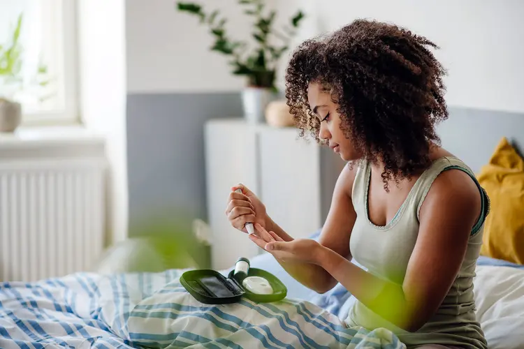 photo of young woman testing blood sugar in bed