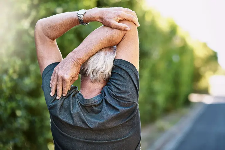photo of an older man doing a PNF stretch; he's holding his right elbow to stretch his upper arm