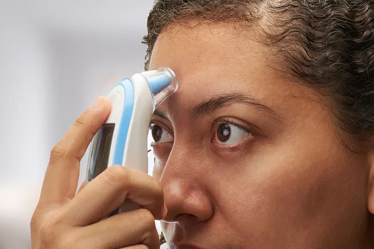 Someone checking their temperature using a temporal artery thermometer