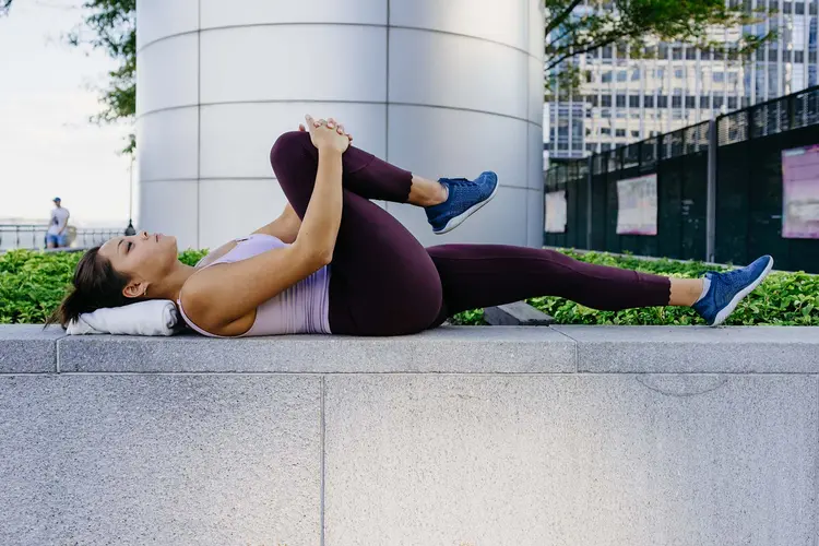 photo of woman holding her right knee against her chest to stretch her lower back, also called a PNF stretch 