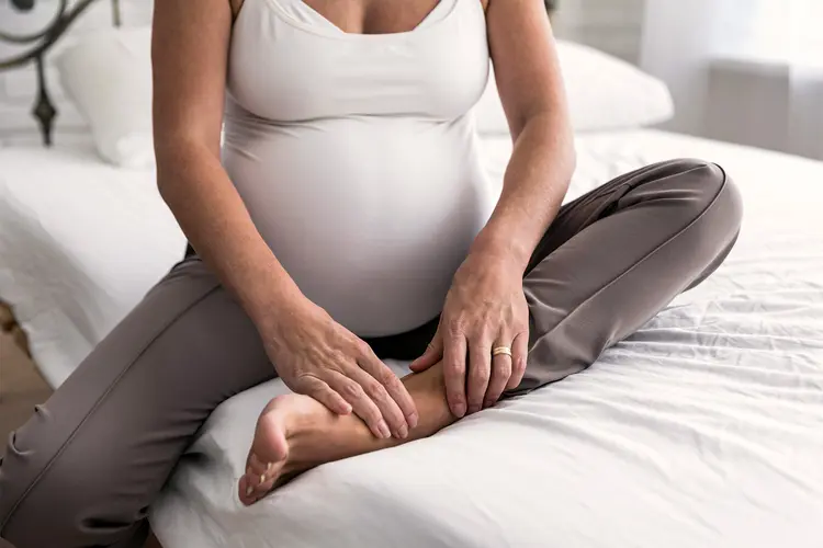 photo of pregnant woman holding sore ankle