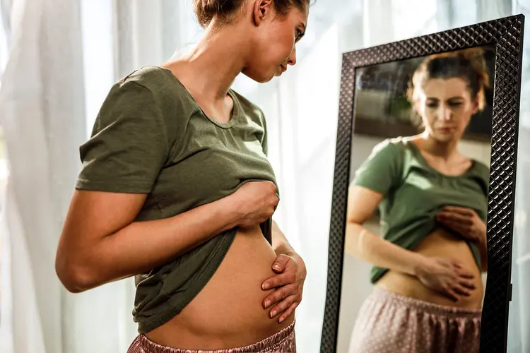 photo of woman looking at bloated belly in mirror