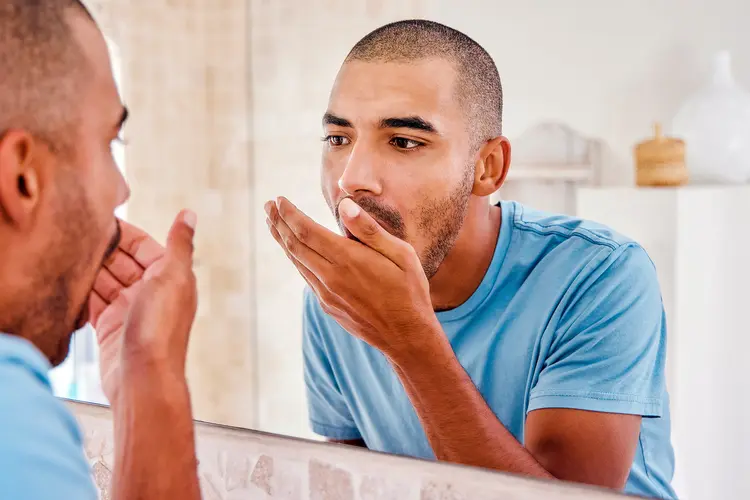 photo of young man smelling his breath in front of mirror