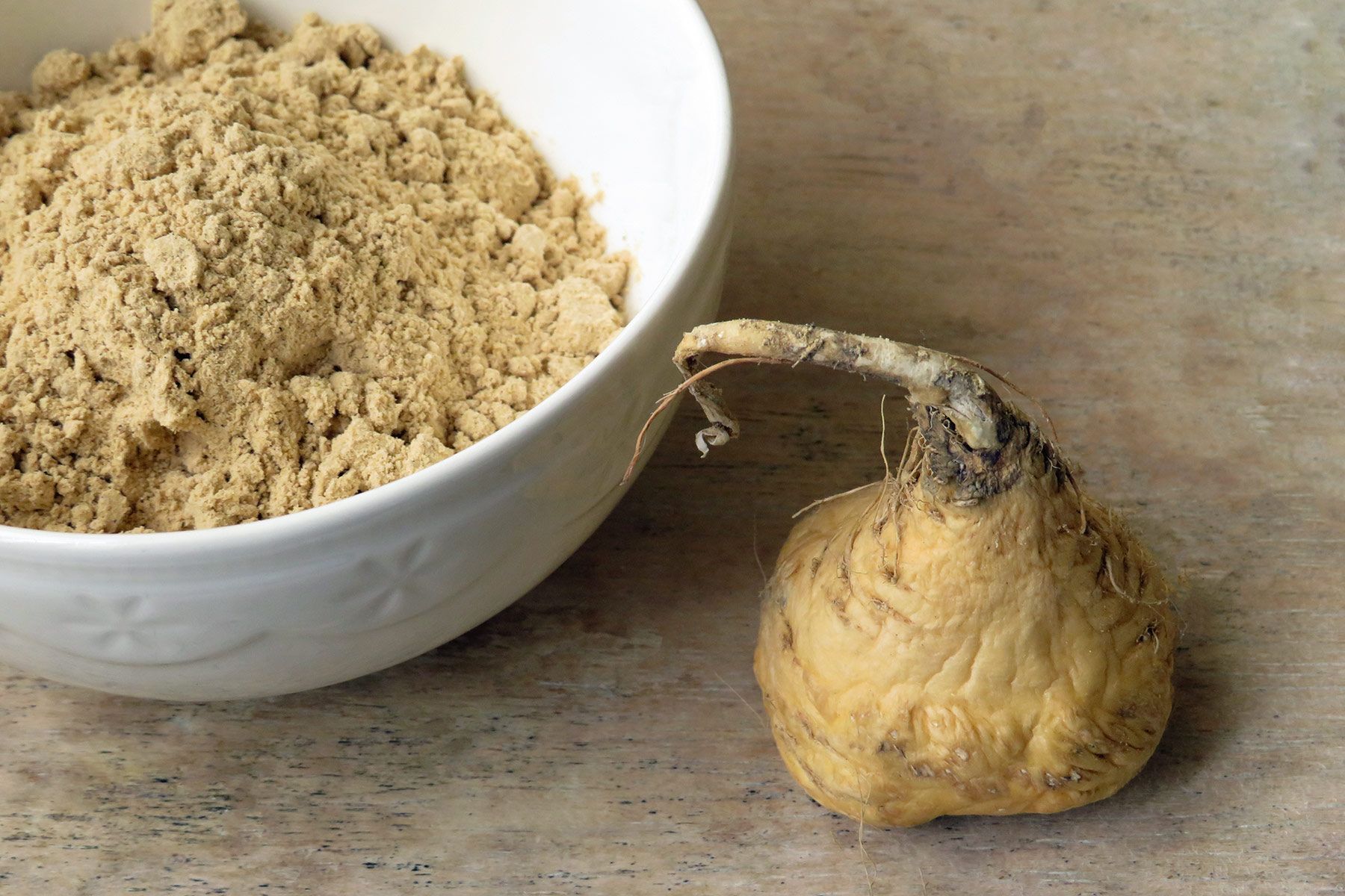 bowl of maca powder and whole maca root on wooden surface