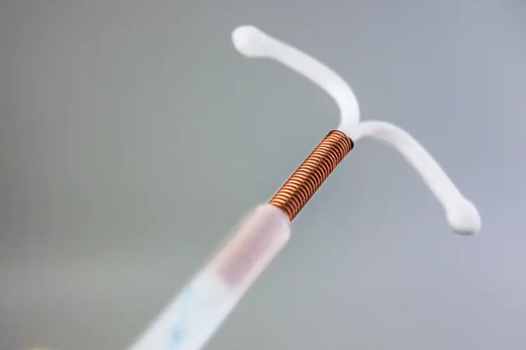 photo of Copper Intrauterine device, the white t-shaped plastic is wrapped in golden copper wire.
