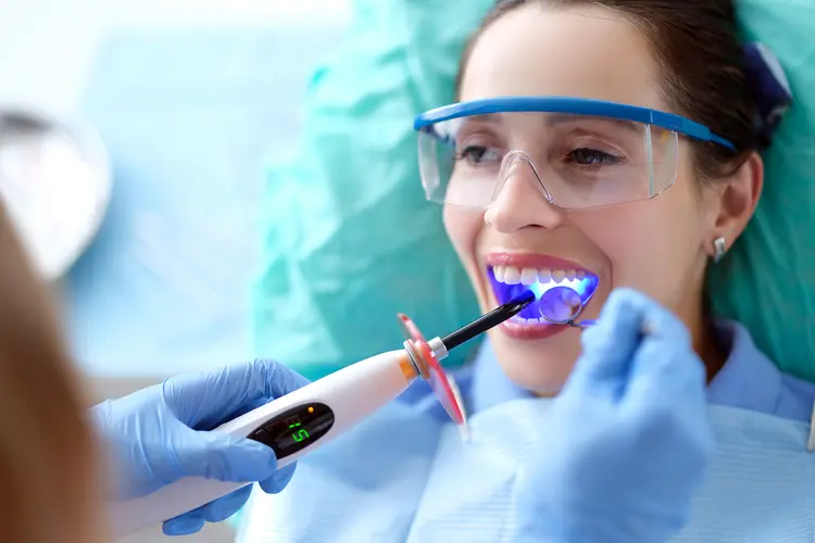 photo of dental bonding as a hygenist shines a blue light on a tooth to bond the resin during the procedure