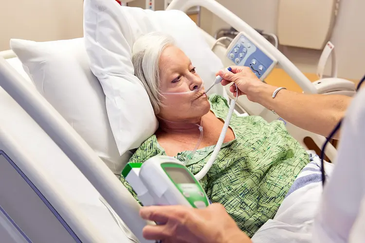 photo of nurse taking temperature of senior woman in hospital bed