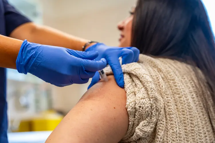 A close-up photo of a nurse's hand injecting vaccine into a woman's shoulder