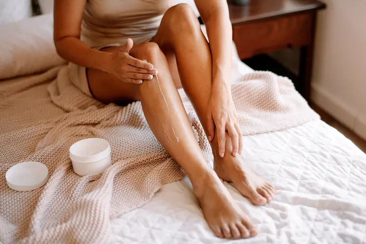 photo of woman applying cream to lower legs