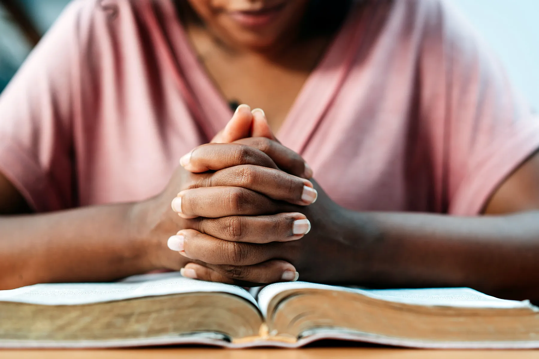 photo of woman praying with the bible on the table