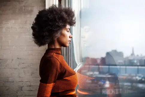 photo of young woman gazing out window at home