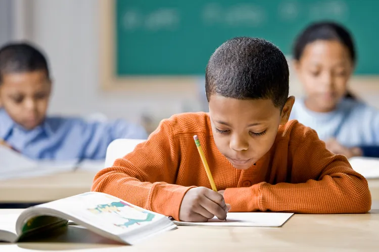 photo of mixed race boy writing at school desk