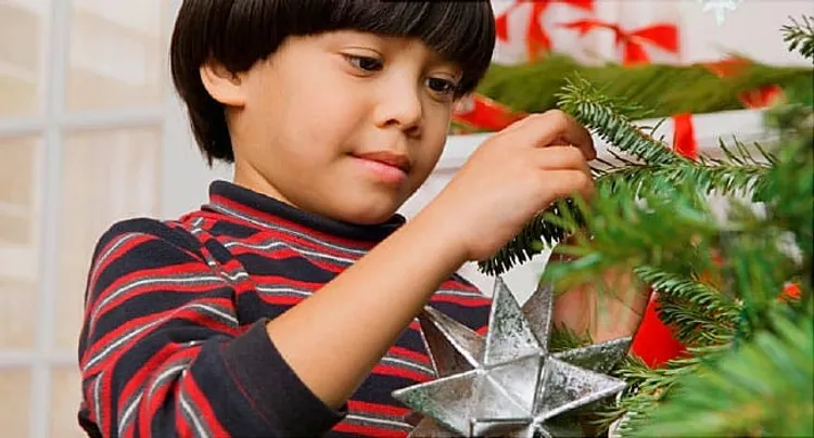 boy putting ornament on christmas tree