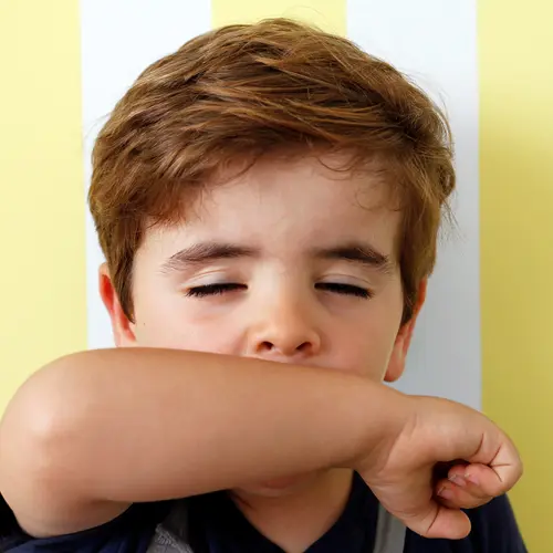 photo of boy sneezing into arm
