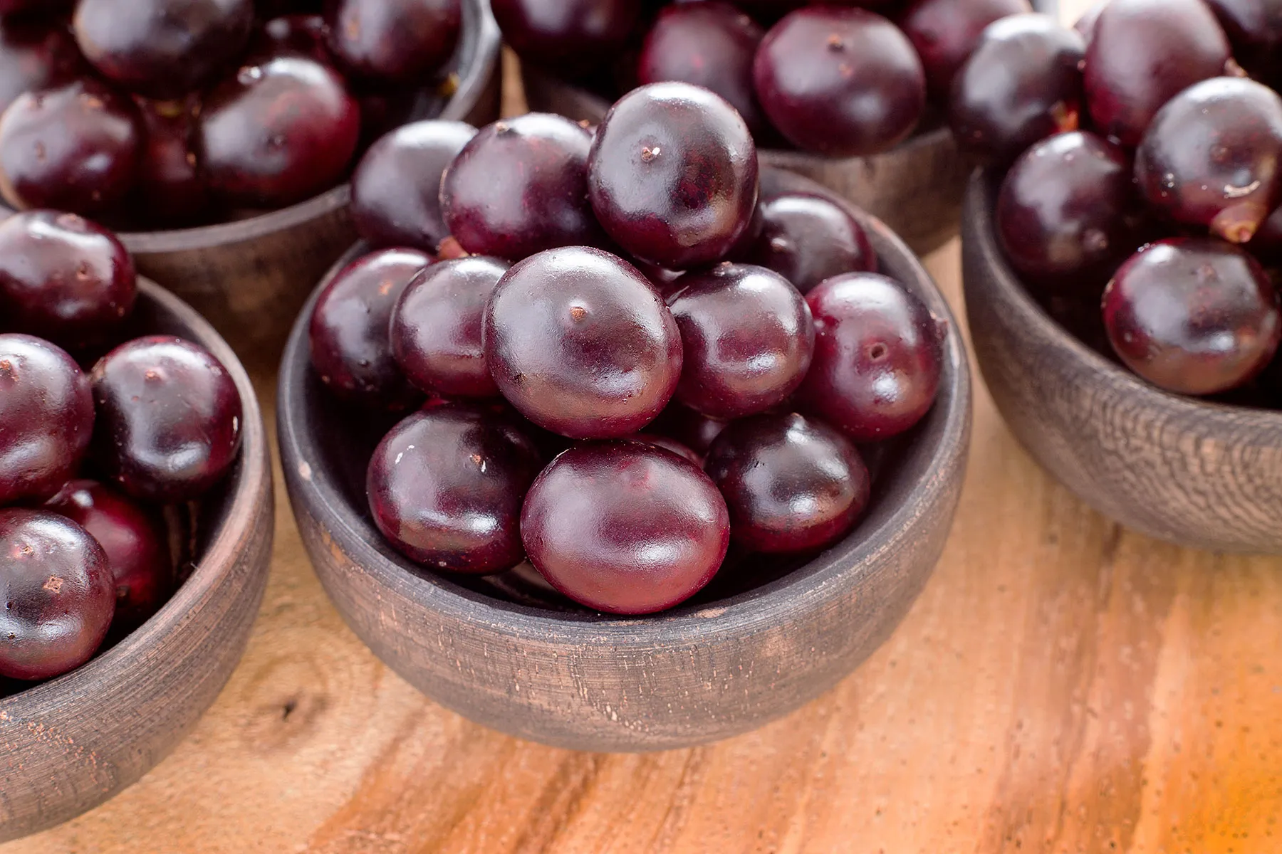 Close-up bowls of dark purple acai-like berries on a wooden surface