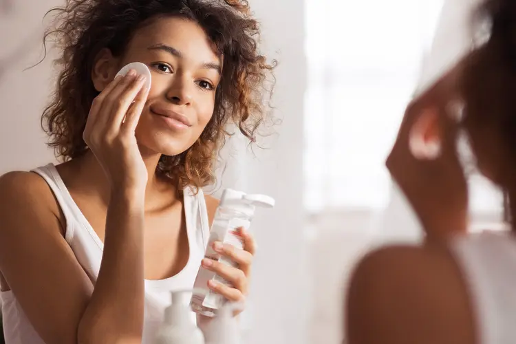 photo of young woman cleaning face with cotton pad