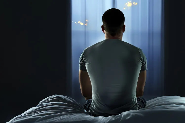 photo of man sitting on edge of bed at night