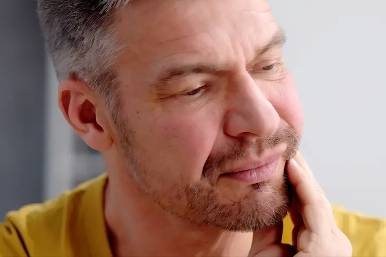 Photo of a man rubbing his jaw, sore from mucositis