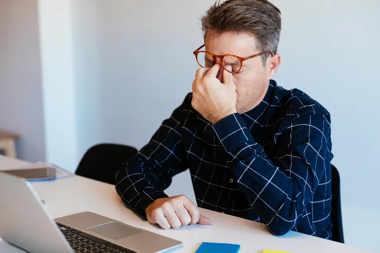 photo of man at desk in office, rubbing his eyes