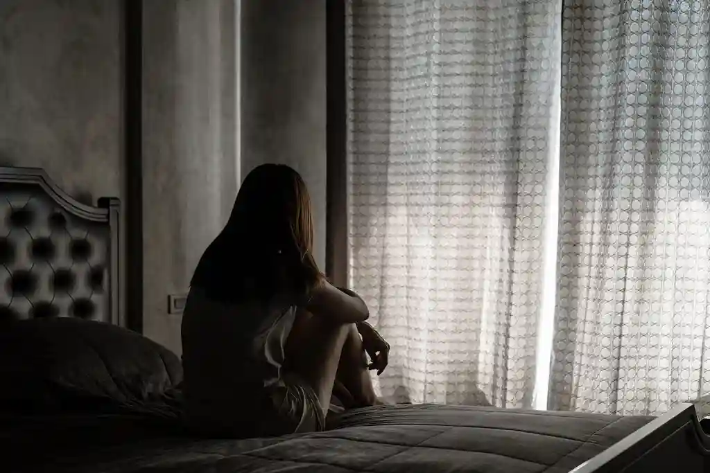 photo of woman sitting on bed in dark bedroom
