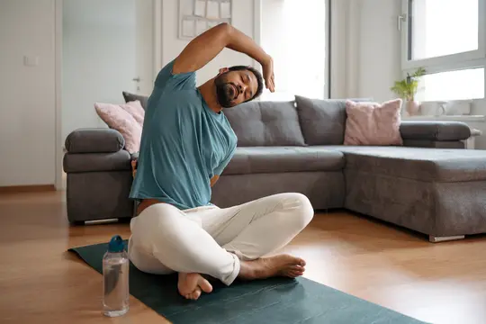 photo of young man stretching / holding yoga pose on floor of living room