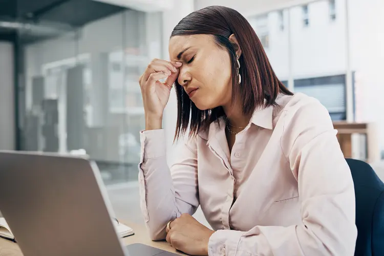 photo of woman with a headache sitting at her desk with a laptop