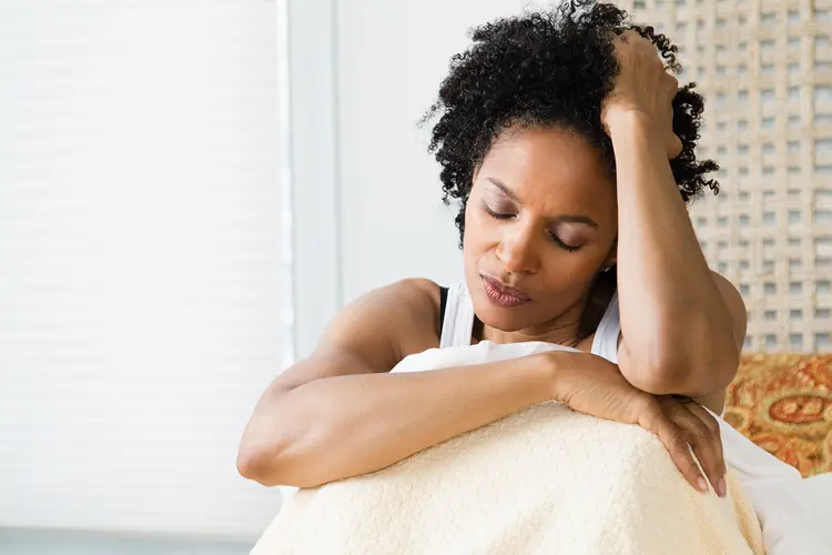 photo of woman sitting up in bed holding her head with eyes closed