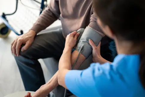 photo of a female nurse in blue scrubs attentively measures the blood pressure of an elderly male patient