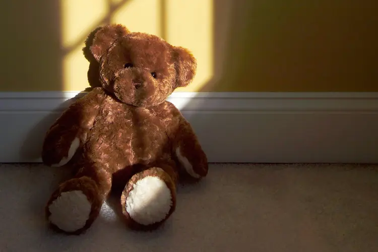 photo of lonely Teddy bear sitting against a yellow wall in the shadows