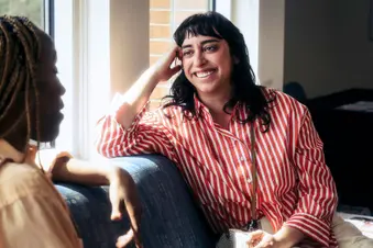 photo of 20s / 30s women smiling as they talk on sofa