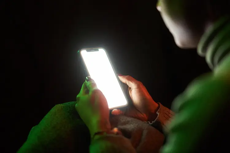 a person wearing green sits in the dark holding a glowing iphone screen and screentime can lead to brain rot