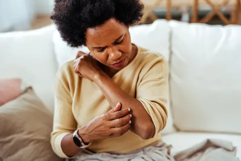 photo of mature woman scratching her forearm at home