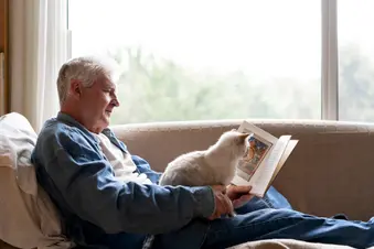 photo of man reading with cat on lap