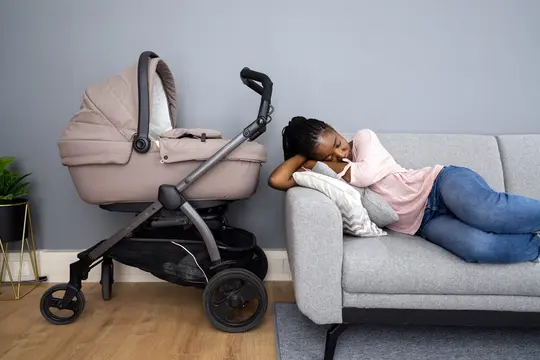 photo of woman sleeping on sofa next to baby in stroller