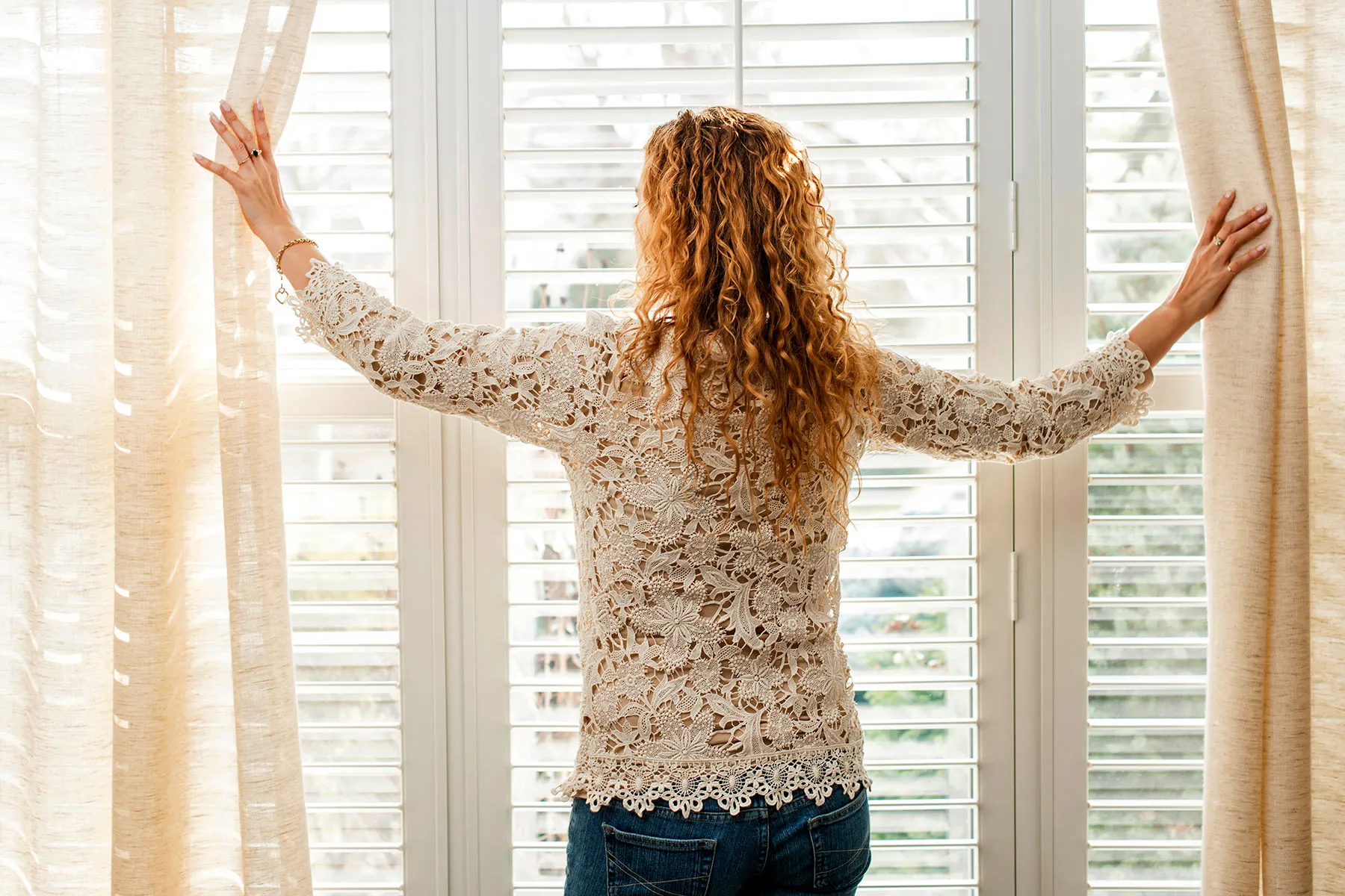 photo of woman opening curtains on sunny day