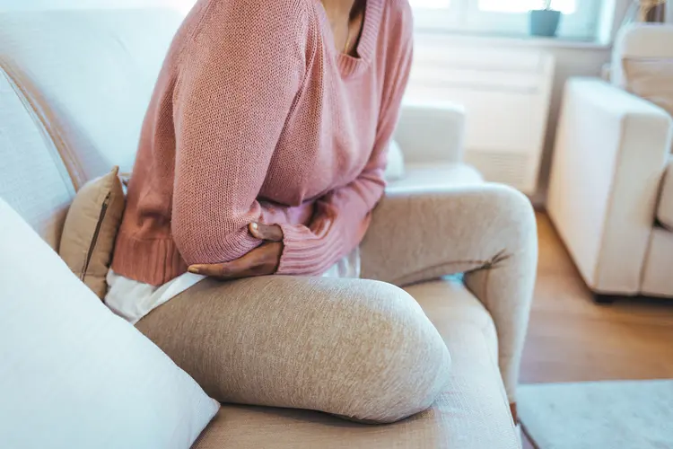 photo of woman holding stomach on couch